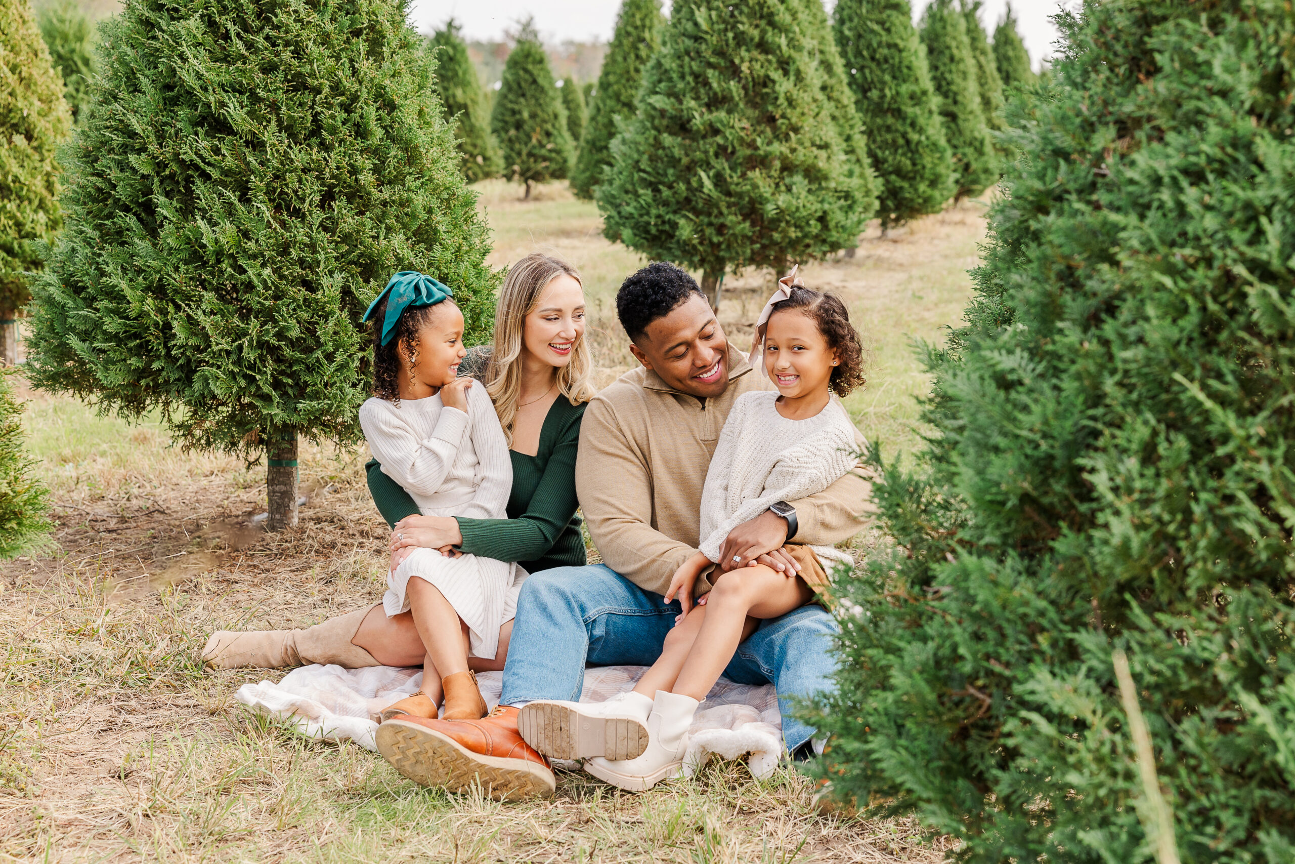 Parents and kids smiling in front of Christmas trees during a mini session at Dewberry Farm.